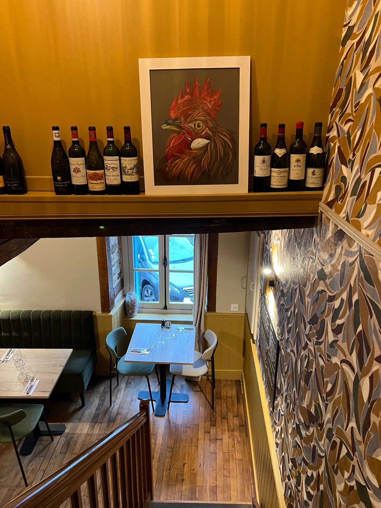 Vue depuis l’escalier sur les tables de Cocorico, les bouteilles et le tableau de coq
